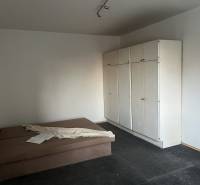A room in a 2-room apartment with an upholstered bed, a white wardrobe, and a dark floor.