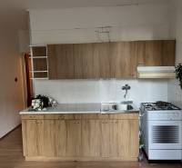 A kitchen in a 2-room apartment with a wood-patterned floor and a gas stove.