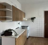 A kitchen in a 2-room apartment with a wood-patterned floor, white tiles, and cabinets.