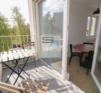 A balcony with seating, a view of greenery, and glass doors to a 2-room apartment.