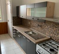 A kitchen in a 2-room apartment with a white tiled floor and a kitchen unit.