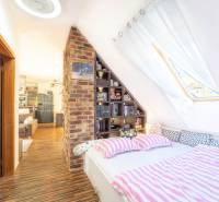 Attic bedroom in a 2-room apartment with brick decor and wood-patterned flooring.