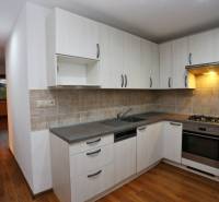 A kitchen with a kitchen unit and a wooden decor floor in a 3-room apartment.