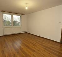 A room with a wooden decor floor in a 3-room apartment, white walls, window, radiator.