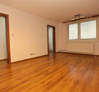 A spacious room with a wooden decor floor and large windows in a 3-room apartment.
