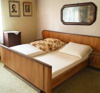 A bedroom with a wooden bed, photographs on the wall, and a mirror in a family house.