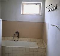 A bathroom in a family house with a bathtub, a window, and a gas heater.