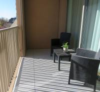 A balcony with rattan furniture in a 3-room apartment, overlooking rooftops and greenery.