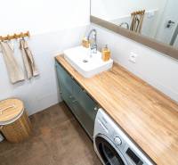 A bathroom with a sink, washing machine, and a floor with a wooden decor in a 3-room apartment.
