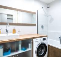 Bathroom with a sink, washing machine, and bathtub in a 3-room apartment, floor with wood decor.