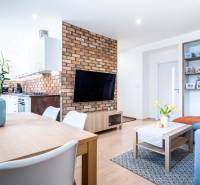 Living room with brick cladding, wood-patterned flooring, and a kitchen in a three-room apartment.