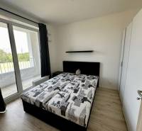 Bedroom in a 2-room apartment with a bed, wardrobe, and balcony with a wooden decor floor.