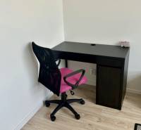 A workspace with a black desk and a pink chair on a wooden-decor floor in a 2-room apartment.