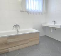 Bathroom in a family house with a bathtub and a sink, light tiles.
