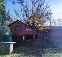 A cottage in Dudince surrounded by trees, with a small stone structure in the garden.