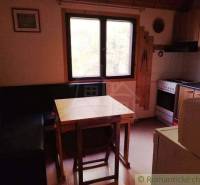 A kitchen in a cottage with a corner bench, table, and stove.