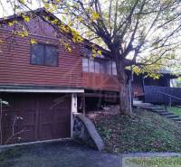 A wooden cottage in Dudince surrounded by trees and a grassy slope.