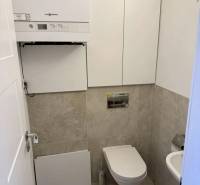 A toilet in a 3-room apartment with a modern wall-mounted boiler and beige tiles.