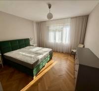 Bedroom with a green bed, wooden decor flooring, opaque curtains, 3-room apartment.