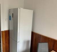 A kitchen in a 2-room apartment with a white refrigerator and wooden wall panels.