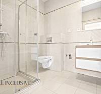 A bathroom in a 2-room apartment with a glass shower enclosure and light tiles.