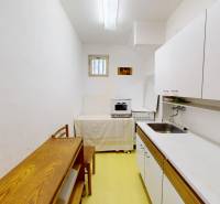A narrow kitchen in a cottage with simple equipment and a wooden table.