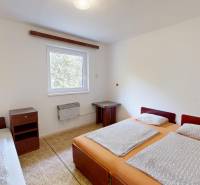 A bedroom in a cottage with three beds, a nightstand, and a window with a view.