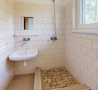 A bathroom in a cabin with a sink, shower, and window, tiled.