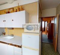 A kitchen in a 3-room apartment with white cabinets and a refrigerator on a floor with a wooden decor.