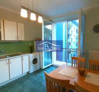 A kitchen in a 2-room apartment with white cabinets, a dining table, and a balcony.