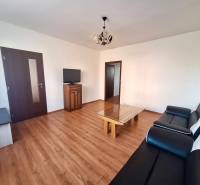 Living room in a three-room apartment with a wooden decor floor, black sofa, and television.