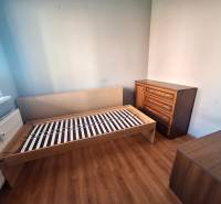 A room in a 3-room apartment with a wooden decor floor, with a bed and a dresser.