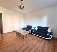 Living room in a three-room apartment with a wooden decor floor and black seating furniture.
