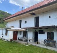 A country cottage with a red roof and a terrace, surrounded by a green lawn and nature.