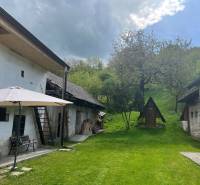 The yard of an older cottage with a gazebo on a bench, a garden in a natural setting on a hill.