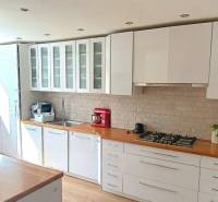 A kitchen in a 3-room apartment with white furniture and a stove, flooring with a wooden decor.