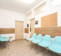 A waiting room with blue chairs, a cork bulletin board, and a wooden-patterned floor in an office.