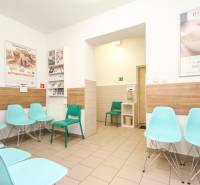 A waiting room with turquoise chairs, walls with wooden decor, medical posters on the walls.