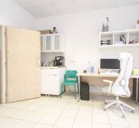 An office with a computer, a white chair, shelves, and a sink.