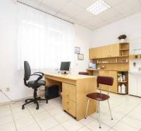 An office with a computer, desk, and chair, bright interior, shelves, and a sink.