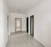 A hallway of a family house with tiles and white walls leading to a door.