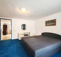 A bedroom in a family house with a large bed, a blue carpet, and a painting on the wall.