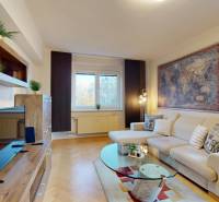 Living room in a two-room apartment with a sofa, TV, and wooden decor flooring.