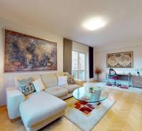Living room of a two-room apartment with a wooden decor floor, sofa, and desk.