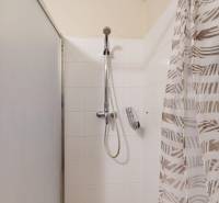 A bathroom in a two-room apartment with white tiles and a shower corner.