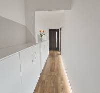 A narrow corridor with white furniture and decoration, a floor with a wooden decor in a 3-room apartment.