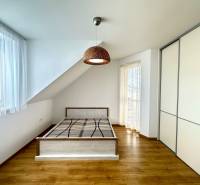 A bright room with a bed, built-in wardrobe, and wood-decorated floor in a family house.