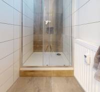 A bathroom with a shower, white tiles, and a floor with a wooden decor.