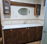 A bathroom in a family house with wooden cabinets, an oval mirror, and ceramic tiles.