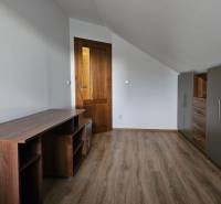 A room in a family house with furniture, white walls, and a wood-patterned floor.
